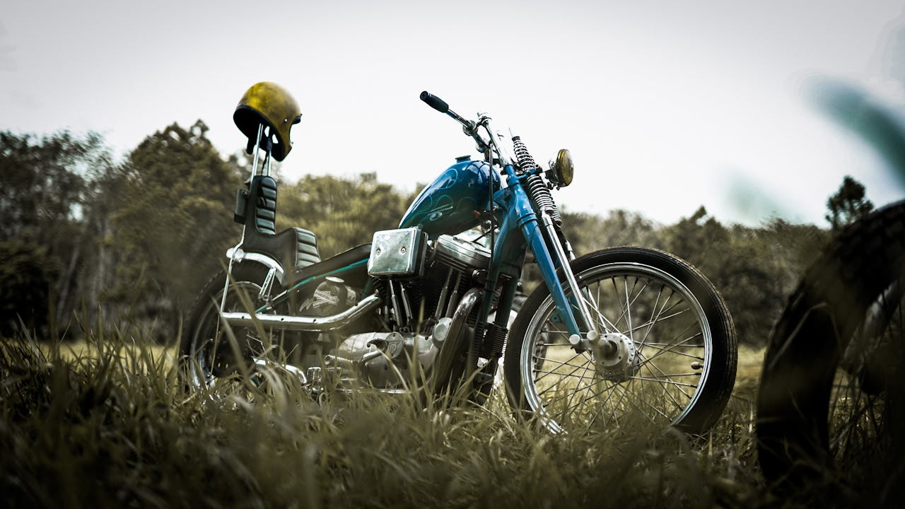 about-01 A classic chopper motorcycle parked on a grassy field with a helmet on the handlebars, under a cloudy sky.