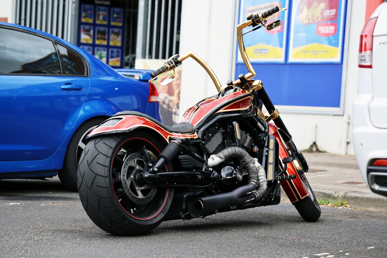 services-02 Vivid image of a custom motorcycle with golden handlebars parked between two cars on a city street.