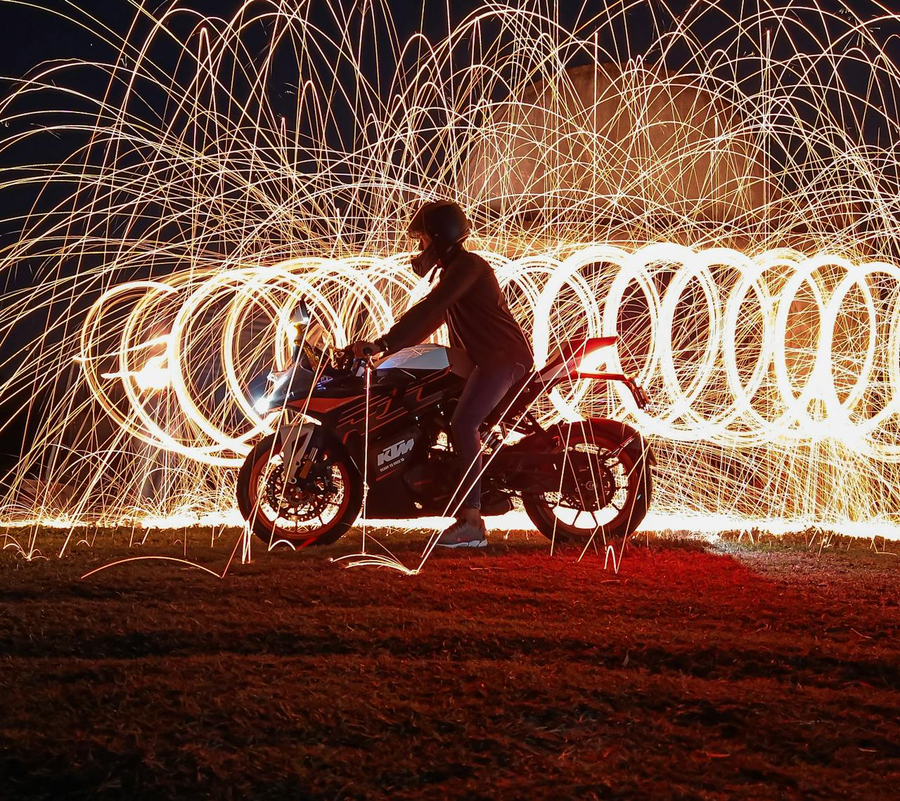 gallery-2 Dramatic motorcycle silhouette amid swirling steel wool sparks, creating a captivating night scene.