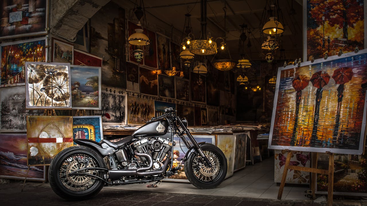 hero-img-01 A vintage motorcycle displayed in an art gallery surrounded by paintings and chandeliers.